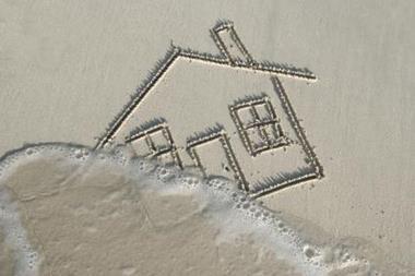 House drawn in sand being washed away by tide